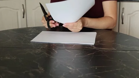 A girl at the kitchen table cuts white paper with scissors Stock Footage 316791345