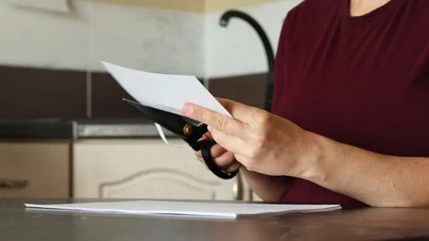 A girl at the kitchen table cuts white paper with scissors Stock Footage 316791474