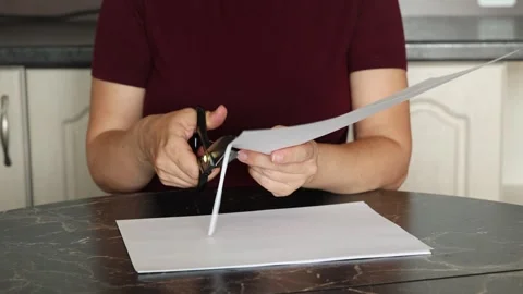 A girl at the kitchen table cuts white paper with scissors Stock Footage 316791720