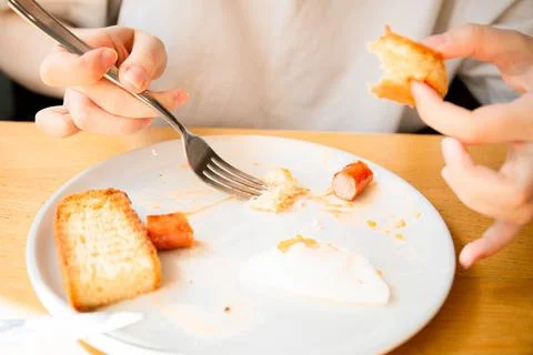A girl with a knife and fork eats an English breakfast fresh tomatoes scrambl Stock Photos