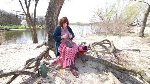 A girl knits clothes from wool while sitting on the roots of a tree Stock Footage 309233243