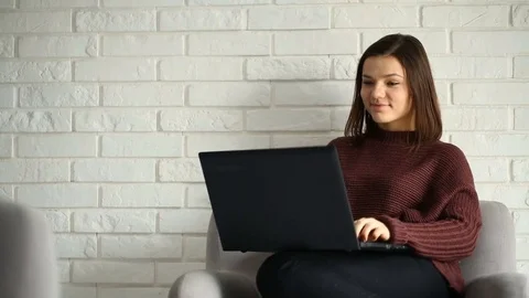 Girl laughing while browsing internet on laptop and sitting on grey armchair Stock Footage 73497269