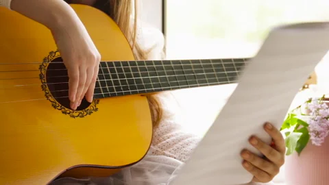 A girl learns to play classical guitar by notes at home near the window Stock Footage 242667284