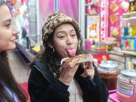 Girl licking a cocholate waffle while standing in a night fair with a friend Stock Photos