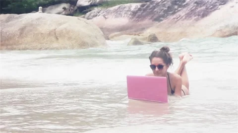 Girl lies on the beach with laptop covering with water Stock Footage 59377629