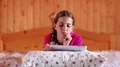 Girl lies on the bed and looks in tablet computer HD Footage