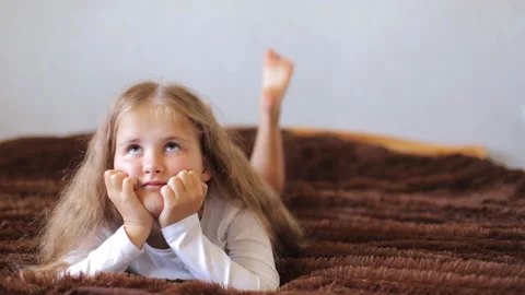The girl lies on the bed in her free time and dreams. The child is lying on the 스톡 동영상 234861973