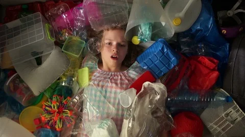 Girl lies in a pile of multi-colored garbage, a plastic bag falls on top of her Stock Footage 106928710