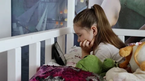 The girl lies on the white bed and looks at the tablet. She is at home Vidéo 131856853