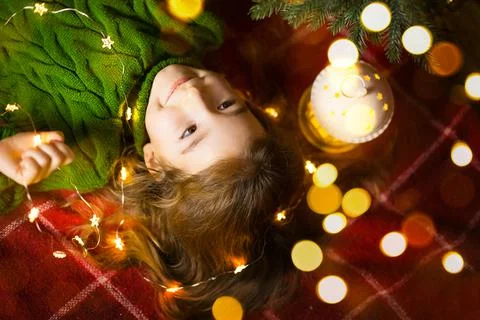 A girl with long hair and garlands lies on a red plaid under a Christmas tree Stock Photos