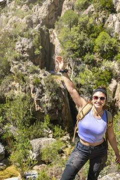 Girl looking at camera backpack pointing with arm a waterfall from the top .. Stock Photos