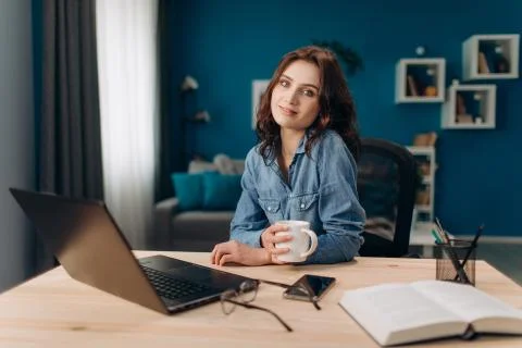 Girl looking at camera while sitting at table with laptop Stock Photos