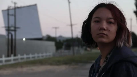 Girl looking at camera while standing by drive in theatre Stock Footage 150383337