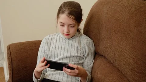 Girl looking at smartphone while sitting on couch. Kid focused on mobile device Stock Footage 309394933