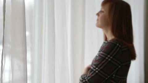 The girl is looking at the snowfall outside the window 스톡 동영상 87603502