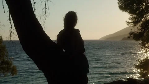 A girl looks at the sunset in the rays of the setting sun on the seashore. Stock Footage 295997236