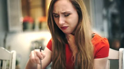 Girl looks worried while eating lunch in the cafe and having sore throat, steady Stock Footage