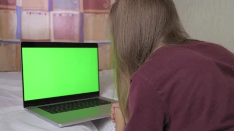 A girl is lying on the bed, in front of her is a laptop with a green screen Video stock 201306233