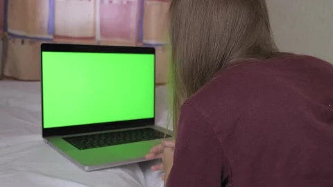 A girl is lying on the bed, in front of her is a laptop with a green screen Video stock 201306255