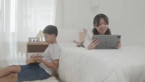 A girl lying in bed playing tablet and a boy sitting beside bed playing guitar. Video stock 240800265