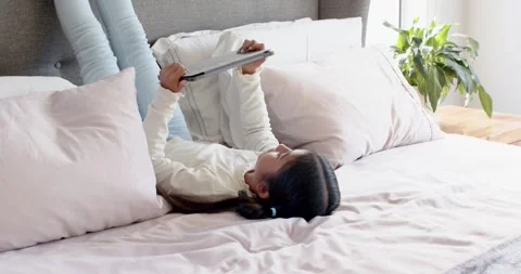 Girl lying on bed propping legs on headboard, holding tablet, tapping scrolling Stock Footage 335808366