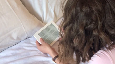 Girl lying on the bed reading an e-book, top view 動画素材 113041231