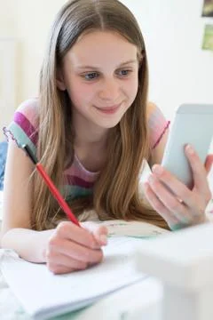 Girl Lying On Bed Using Mobile Phone To Help With Homework Stock Photos
