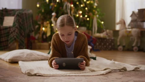 Girl Lying on Floor Using Digital Tablet by Christmas Tree at Home Stock-Footage 346883834