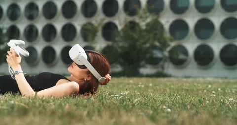 Girl lying on the grass taking off the vr goggles Stock Footage 201134630