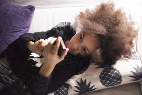 Girl lying on sofa using smartphone Fotos de archivo