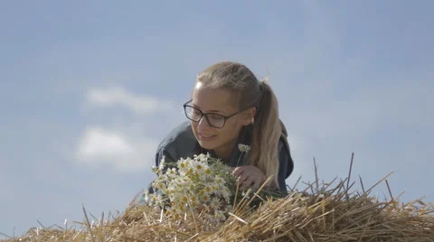Girl lying on a stack of straw with a bouquet of white daisies Stock Footage 67378187