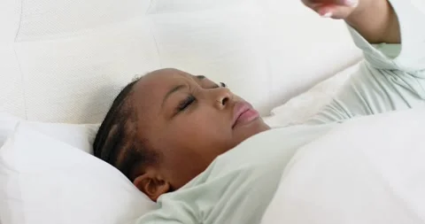 Girl lying on white bed is shielding eyes with right arm against morning light Stock Footage 344325739