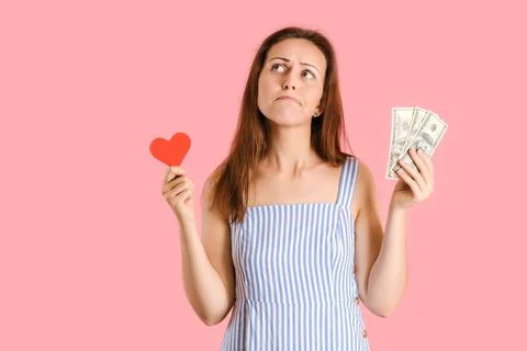 A girl makes a difficult choice between money and love. Studio shot on a pink Stock Photos
