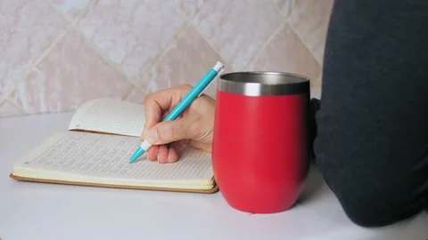 The girl makes a note in a notebook while sitting at the kitchen table and Video stock 211876386