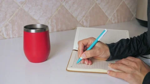 The girl makes a note in a notebook while sitting at the kitchen table and Stock Footage 212616921
