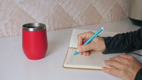 The girl makes a note in a notebook while sitting at the kitchen table and Video stock 213832577