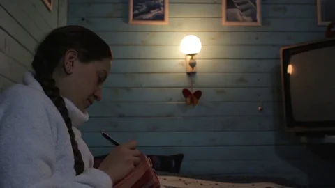 Girl makes notes in a notebook sitting in the room with the light of the lamp Stock Footage 72151322