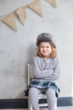 Girl making face while sitting on chair against gray wall Fotos de archivo