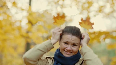 Girl making funny faces at the camera closing herself with autumn leaves Stock Footage 223980321
