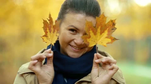 Girl making funny faces at the camera closing herself with autumn leaves Stock Footage 231069669