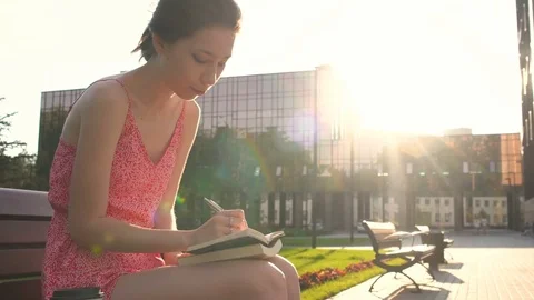 Girl Making Notes at Sunset in Rays of the Sun, writing down her hopes and Stock Footage 77773633