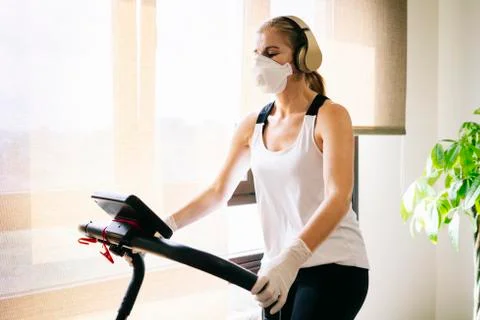 A girl with mask and gloves slim athlete does exercise at home running on the Stock Photos