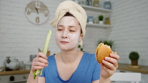 Girl with mask on face smells eats hamburger and celery Stock Footage 101244227