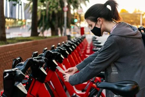 Girl with mask scanning the code to unlock a bike Stock Photos