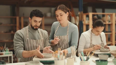 Girl master leaned over to man and helps to sculpting from clay Stock Footage 341783073