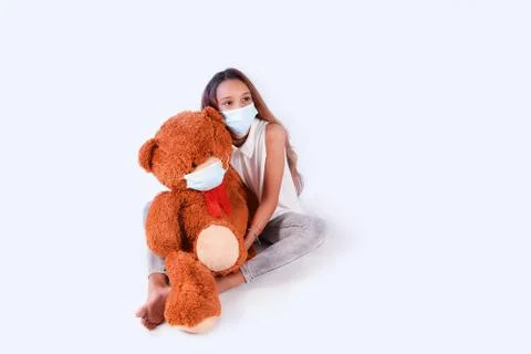 Girl in a medical mask holding a big bear in a surgical mask looking sadly at Stock Photos