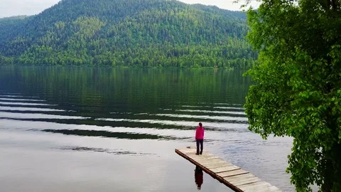 The girl meditates on the pier, on the shore of a mountain lake Stock Footage