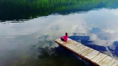 The girl meditates on the pier, on the shore of a mountain lake Stock Footage