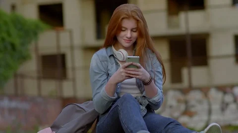 Girl Messaging on Smartphone while Sitting on Skateboard Outdoors Видео 96320020