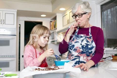 Girl Mixing Cake At Kitchen Counter Whilst Grandmother Licking Her Fingers